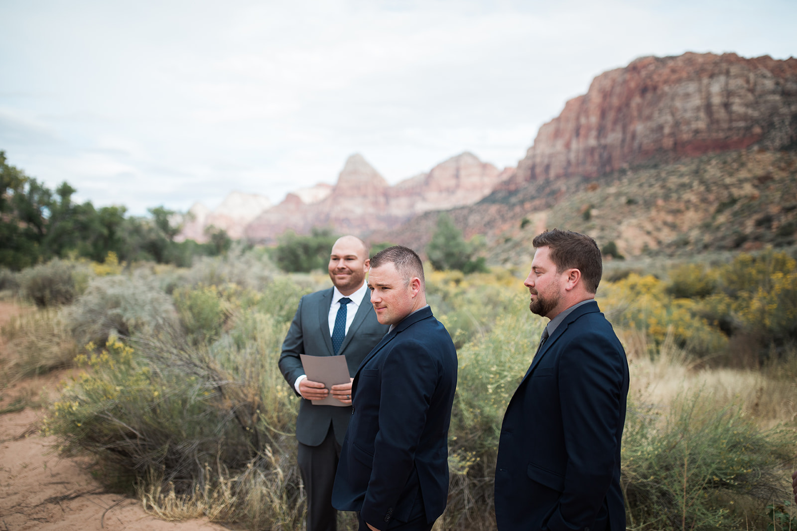 groom watches bride arrive in front of dramatic Zion mountain backdrop