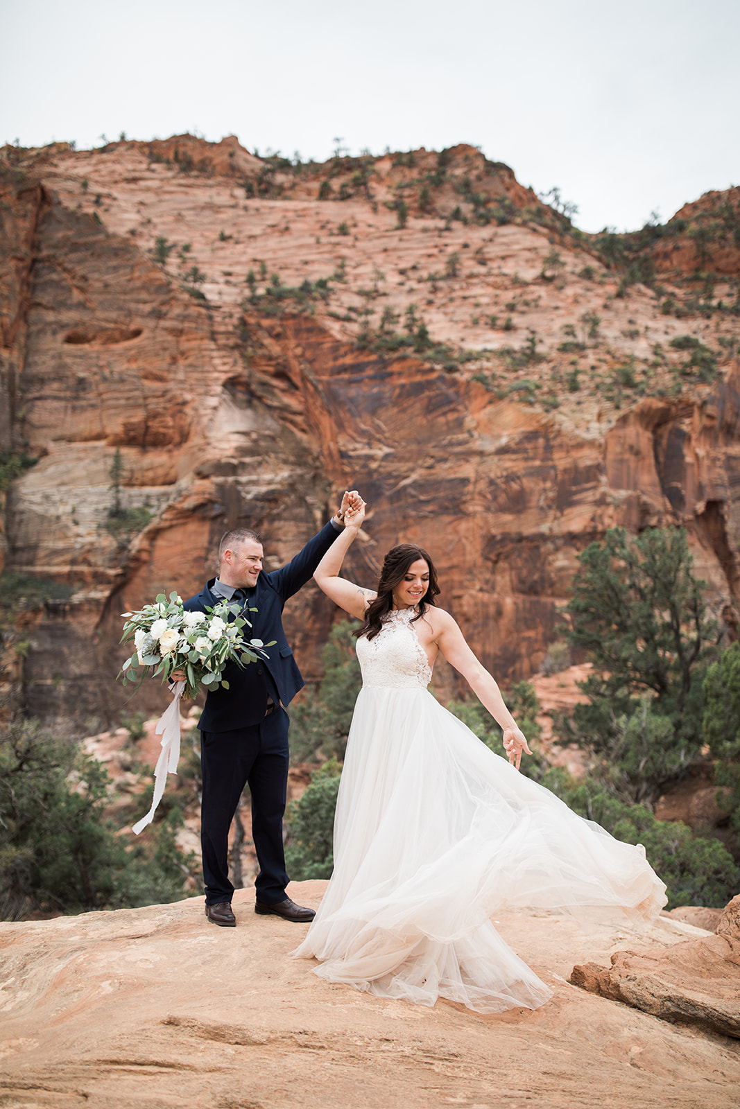 groom spins bride around in front of sandstone
