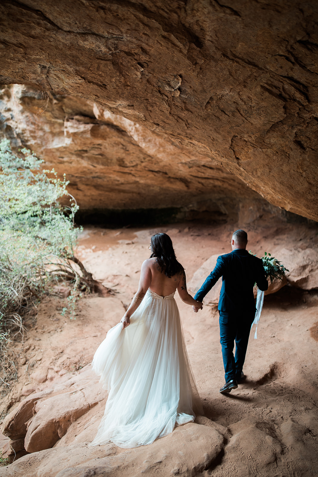 bride and groom walk down into sandstone cave