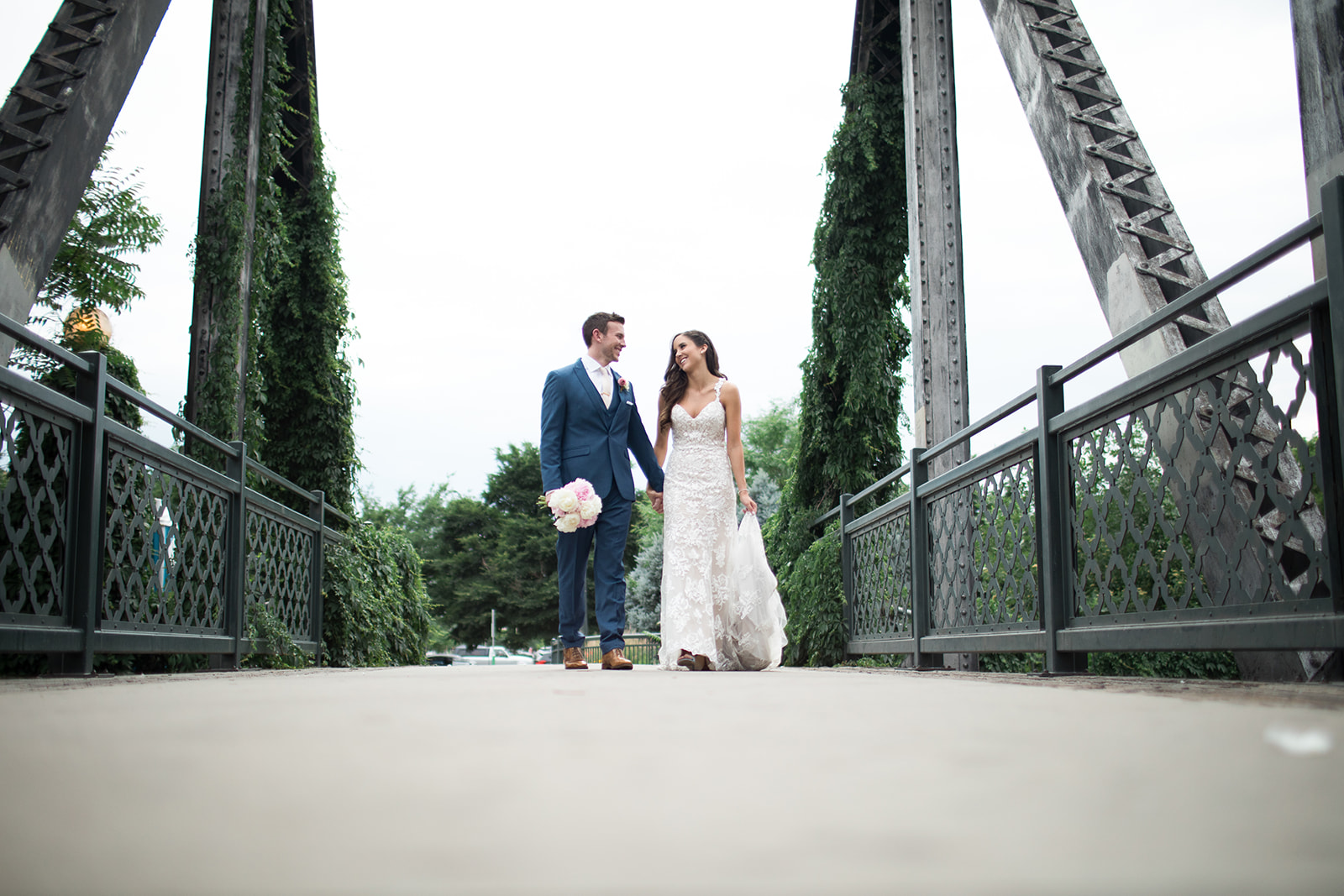bride and groom walking on bridge overlooking Denver skyline