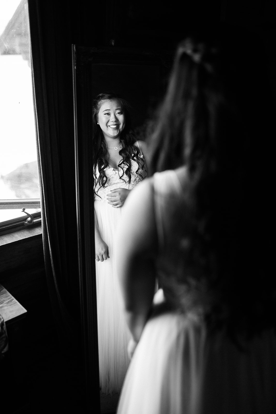 bride looks at self in mirror after putting on wedding dress for Colorado mountain ranch wedding