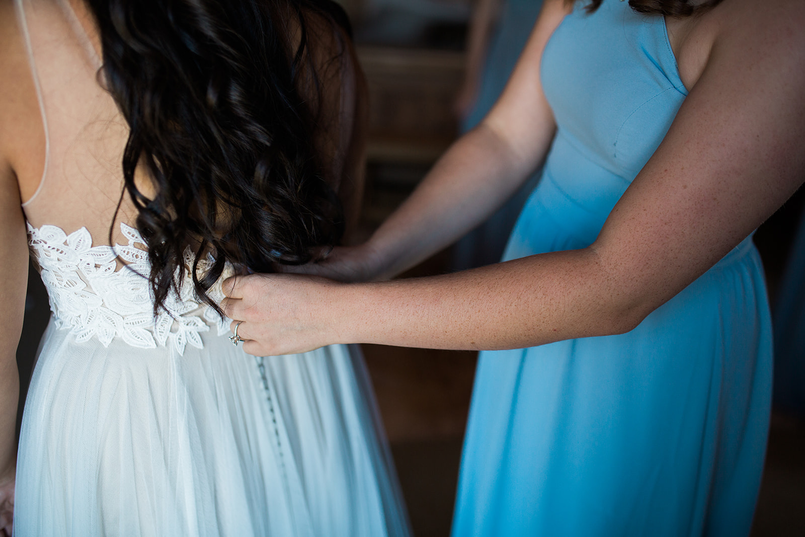 bridesmaid helps bride into wedding dress