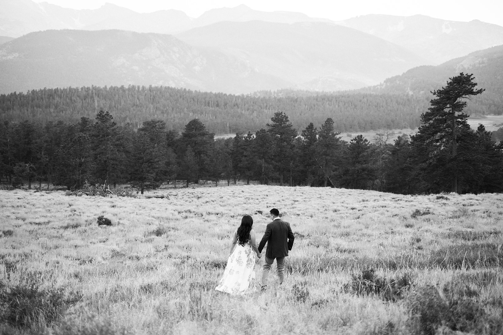 couple walks through RMNP meadow at sunset