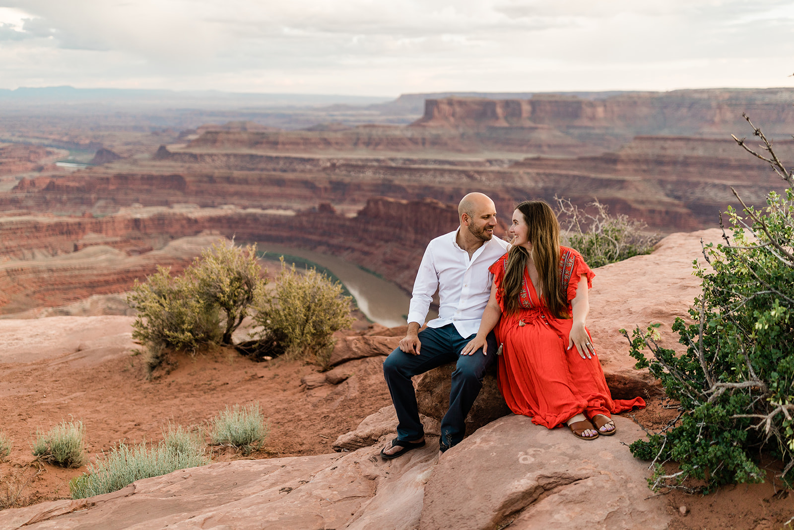 engaged couple sits on rock overlooking Moab dessert