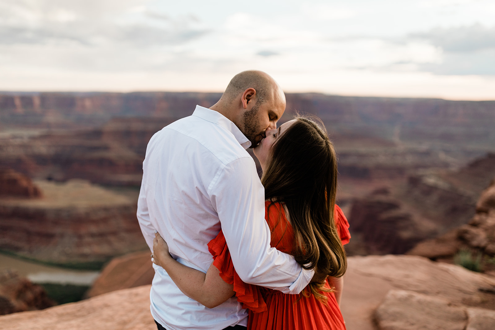 engaged couple hugs and looks out over Moab landscape