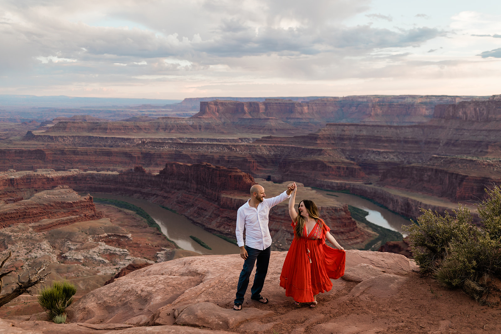 engaged couple dances on top of Moab bluff during adventure photography session with Hazel and Lace Photography