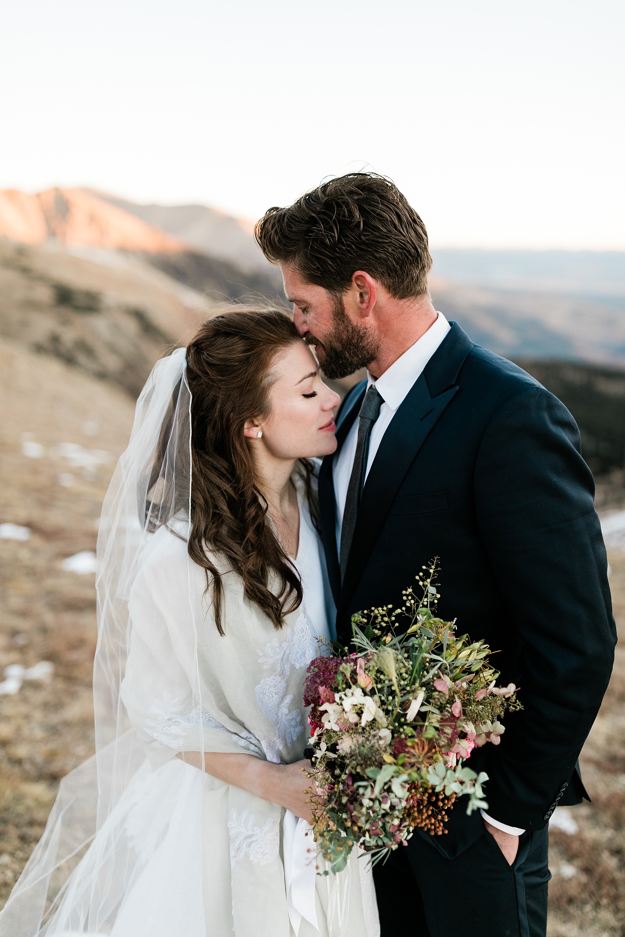 groom kissing bride on forehead on mountain top