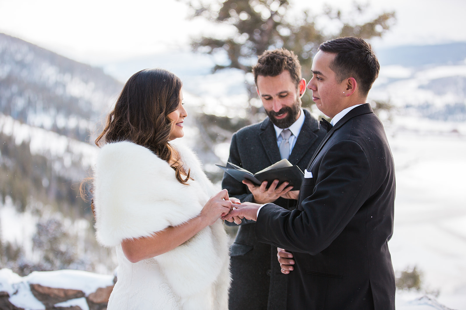 bride puts ring on groom in front of snowy Colorado mountain backdrop