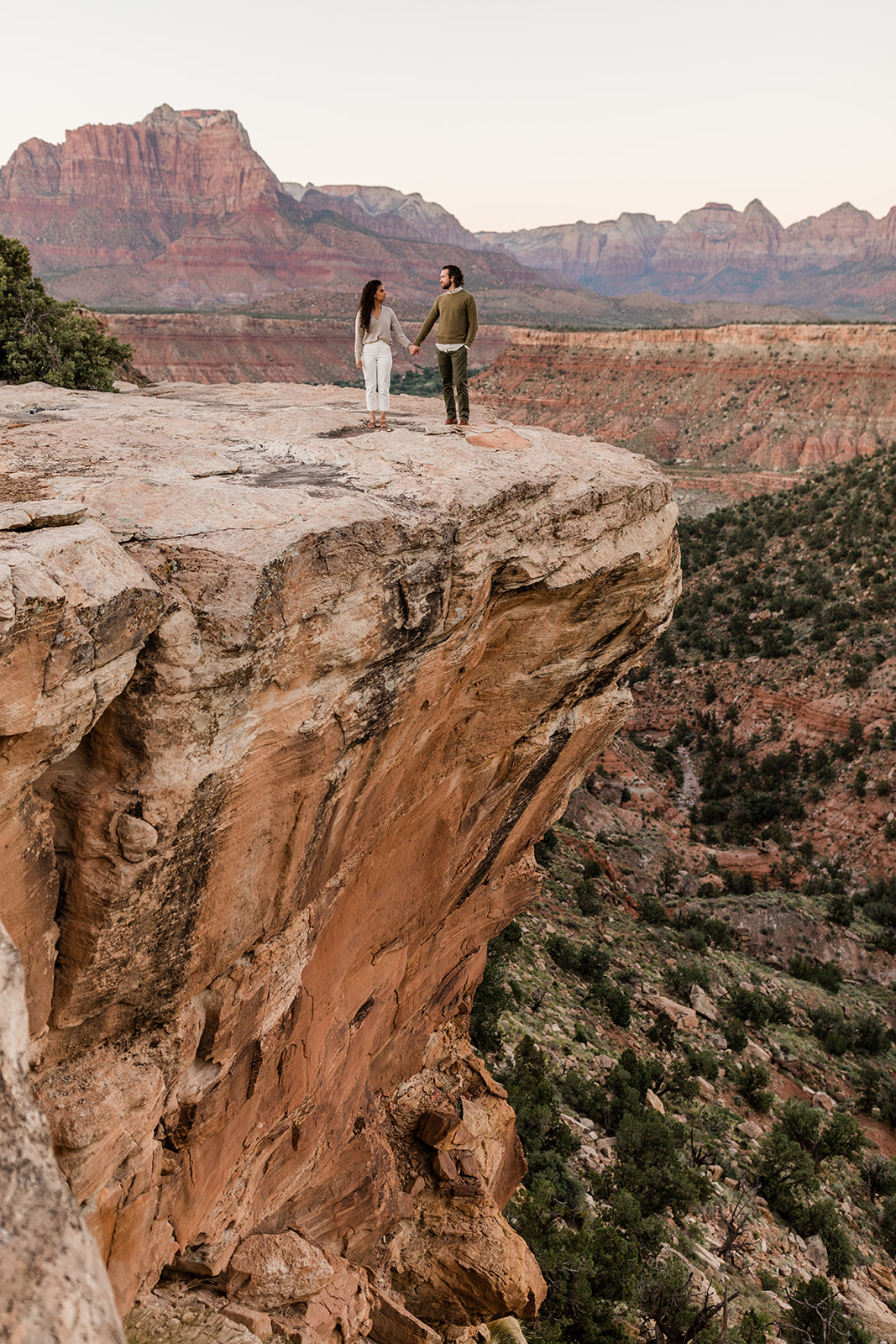 engaged couple stands on rock overlooking Zion National Park
