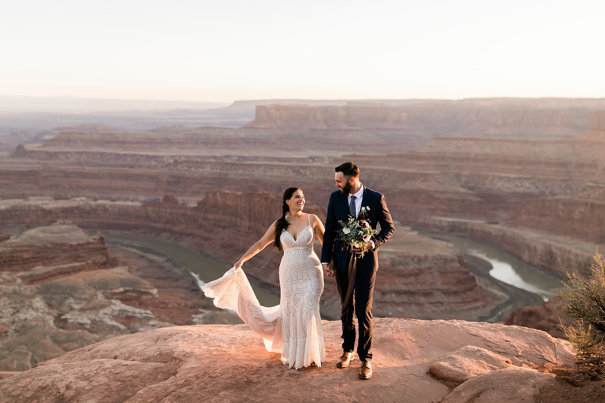 A couple in wedding attire stands in front of a Dead Horse Point Overlook.
