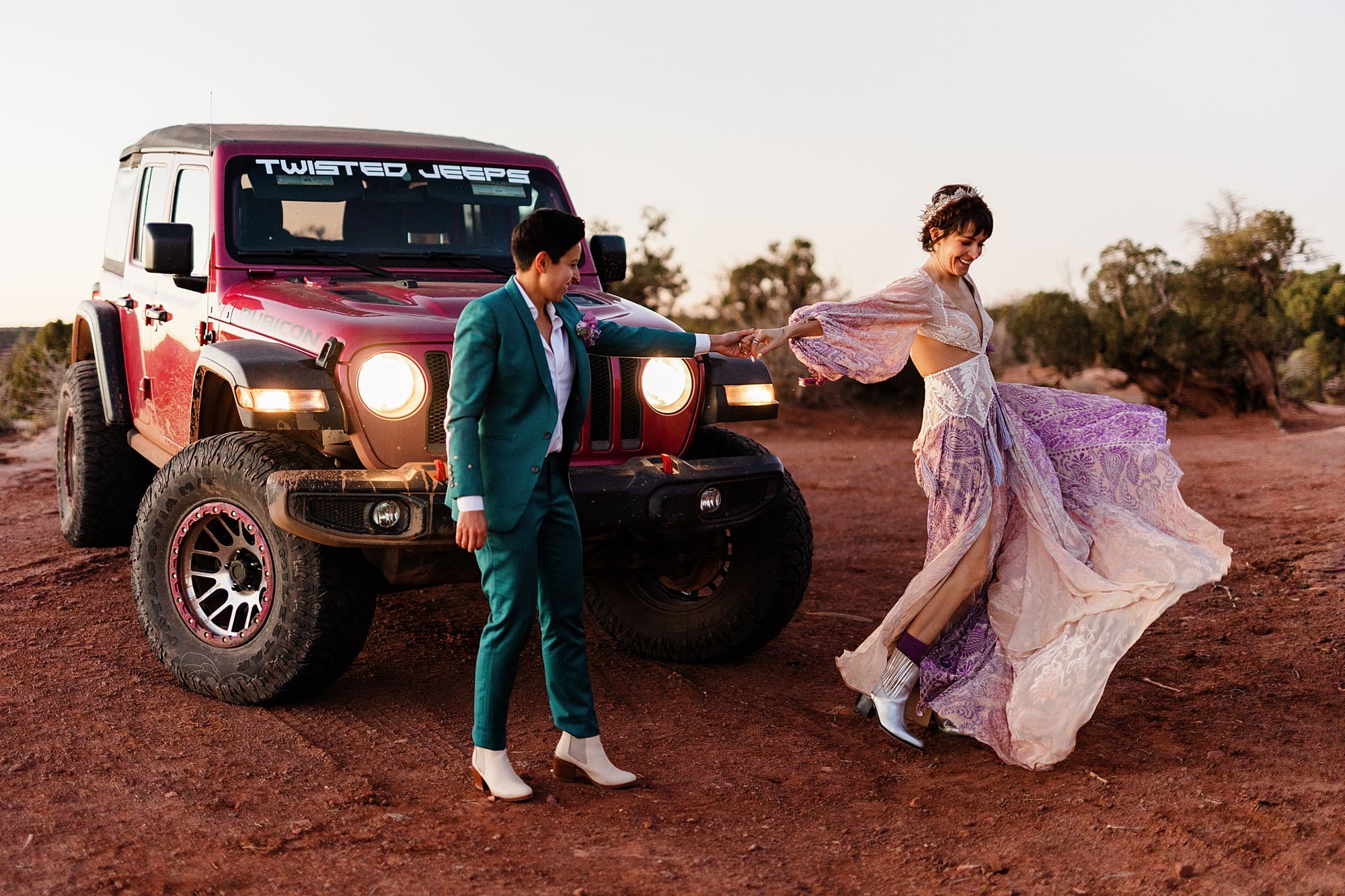 A couple in wedding attire poses in front of an off-roading vehicle in Moab, Utah.