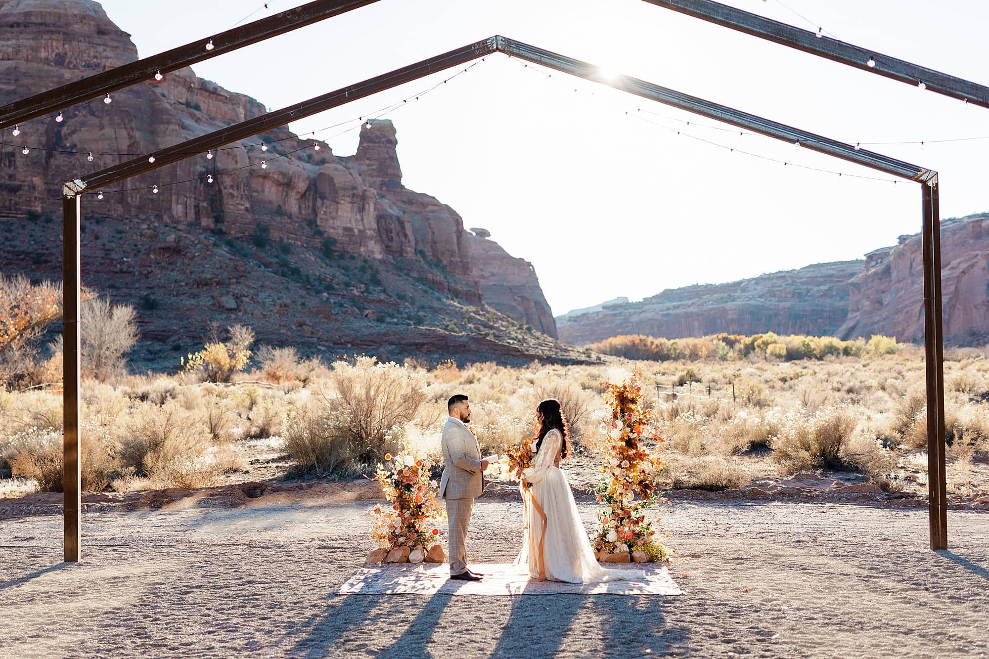 A couple stands beneath a wooden arch as they read their vows in Moab.