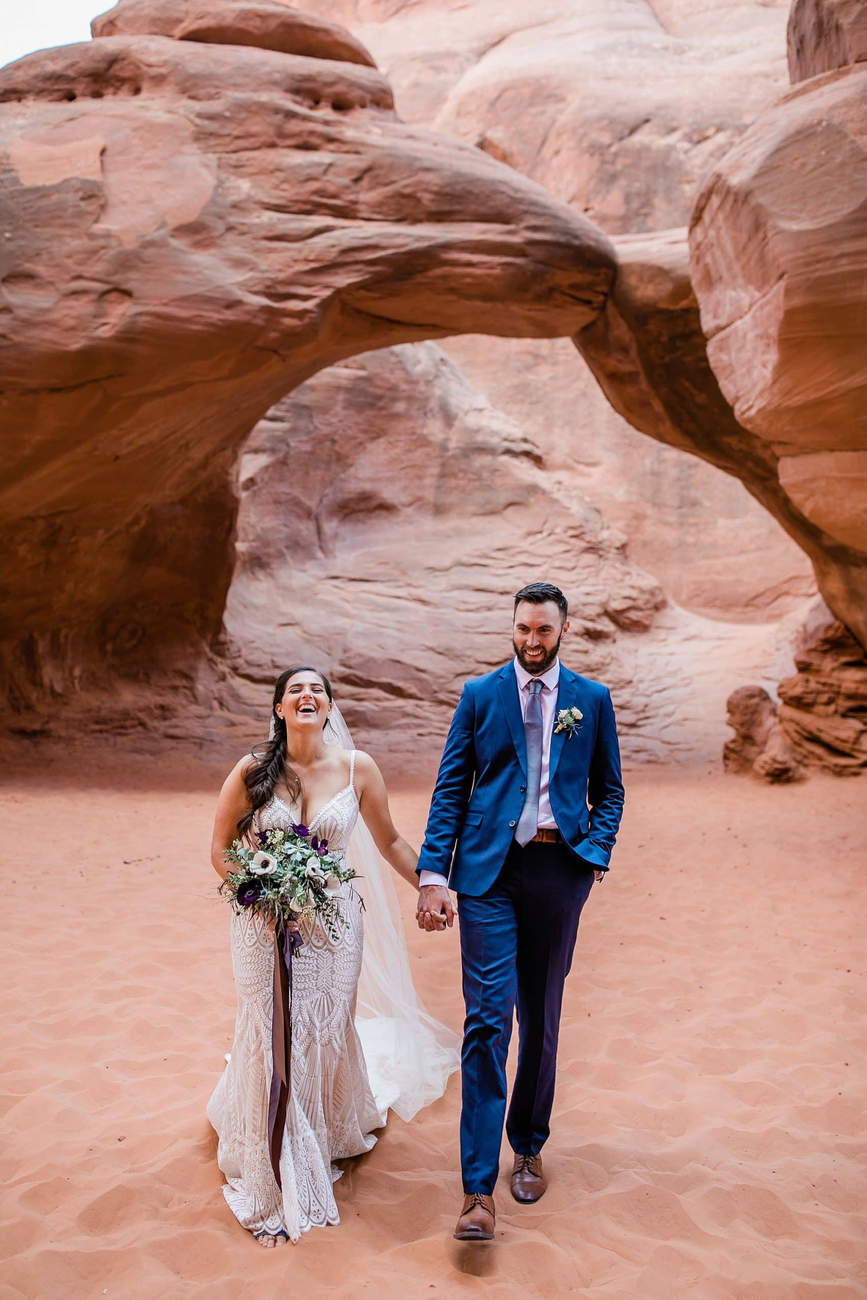 A bride laughs while holding her groom's hand near Sand Dune Arch in Moab, Utah.