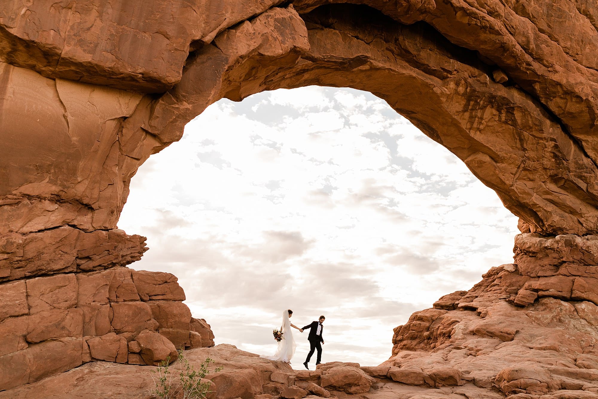A couple holds hands inside an arch in The Windows Section in Moab.