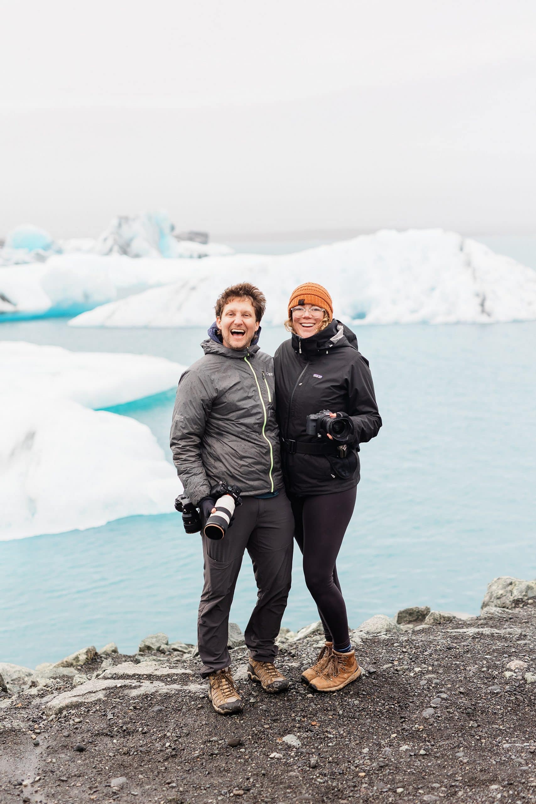 An elopement photographer and elopement videographer pose near a glacier in Iceland