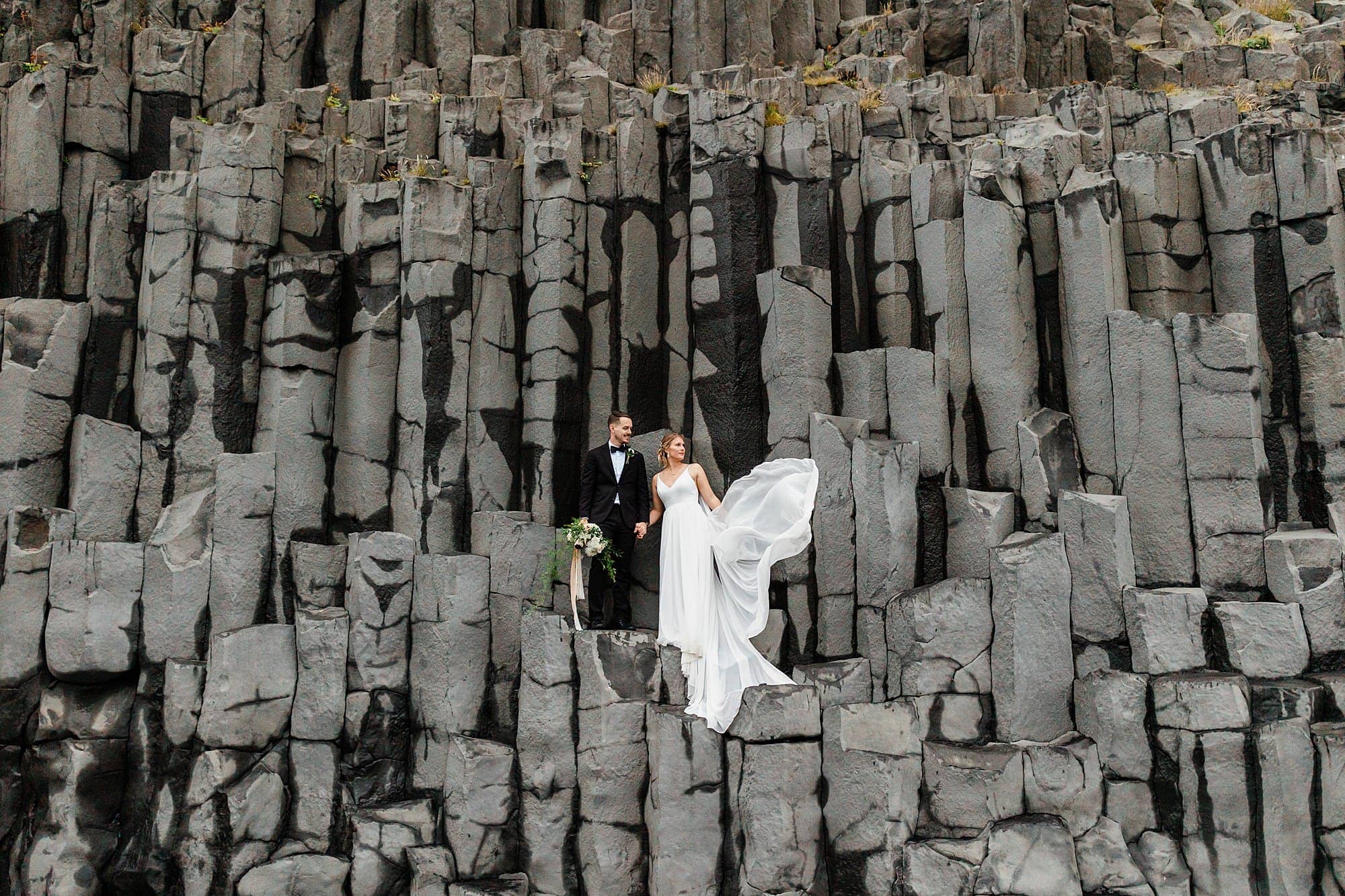 A newly married couple stands on basalt columns at Black Sand Beach in Iceland