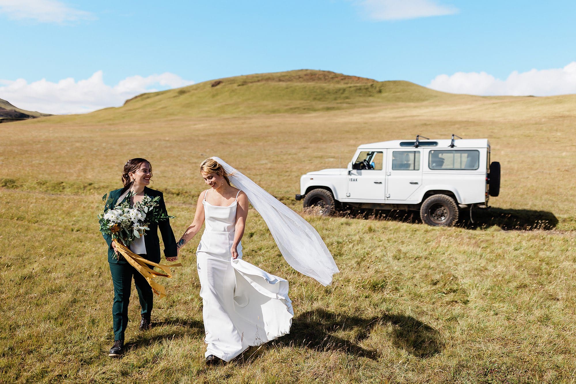 A couple holds hands near a 4x4 as they celebrate in the Icelandic Highlands after their elopement