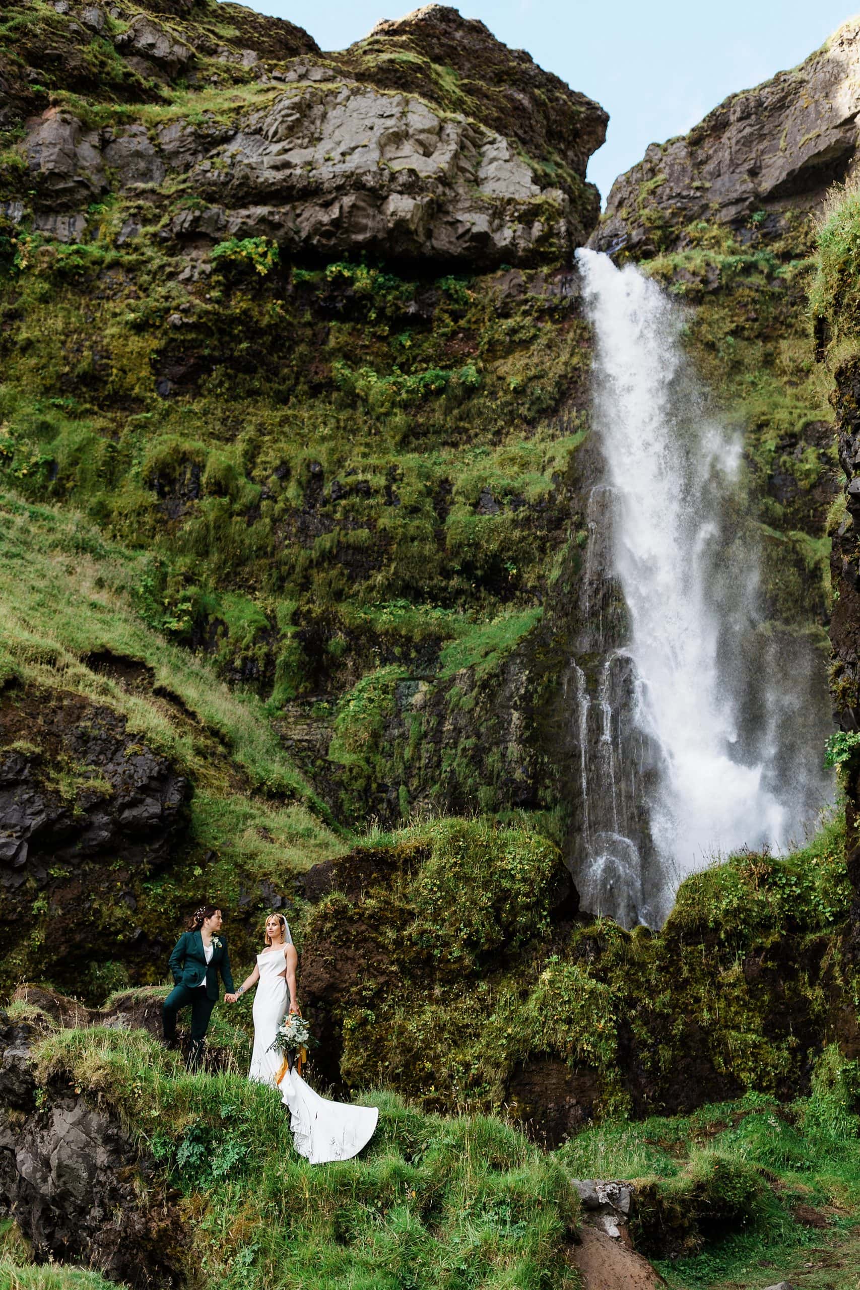 Newlyweds hold hands near a large waterfall after they elope in Iceland