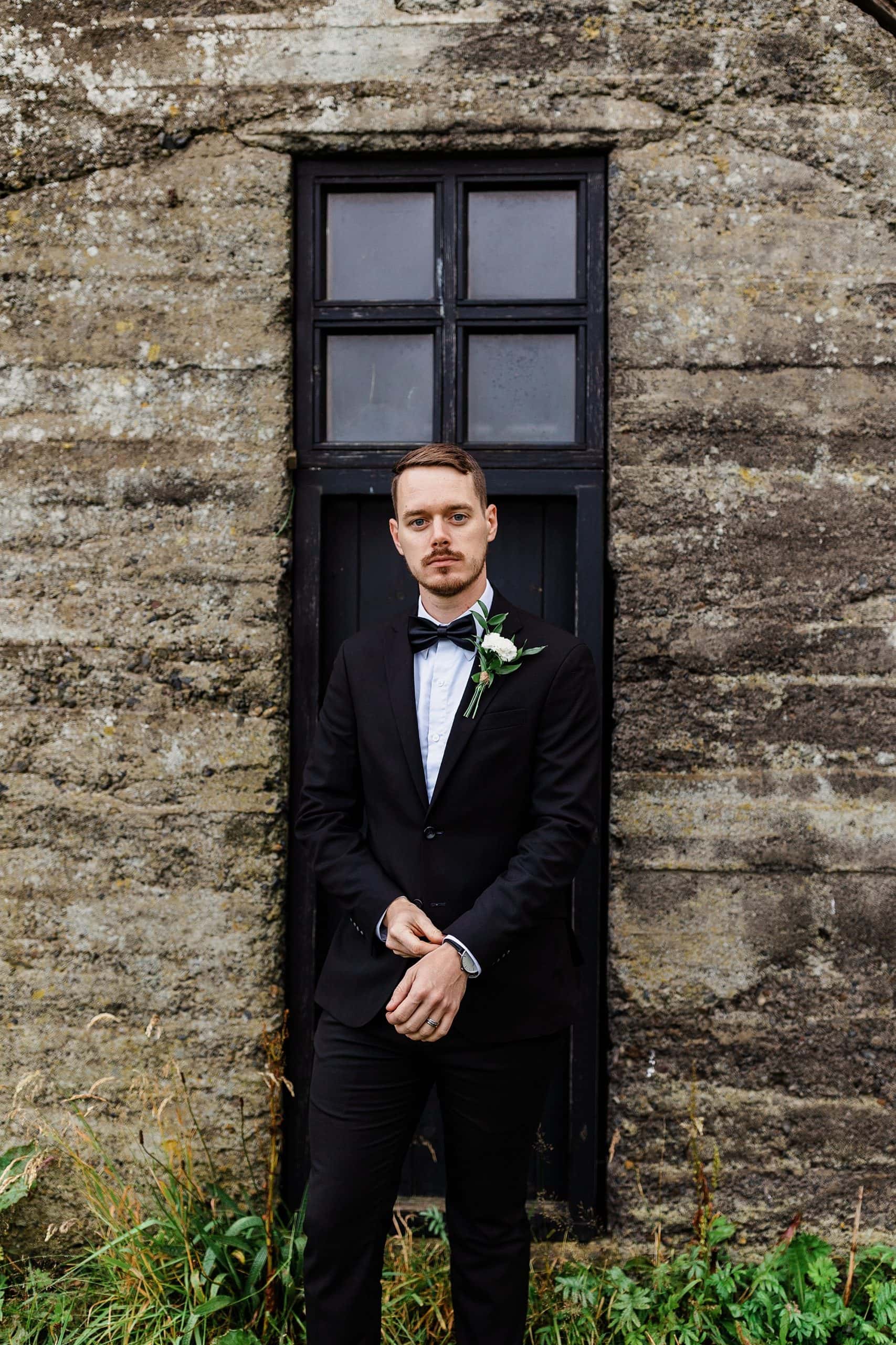 A groom stands in front of a black window in Iceland along Route 1