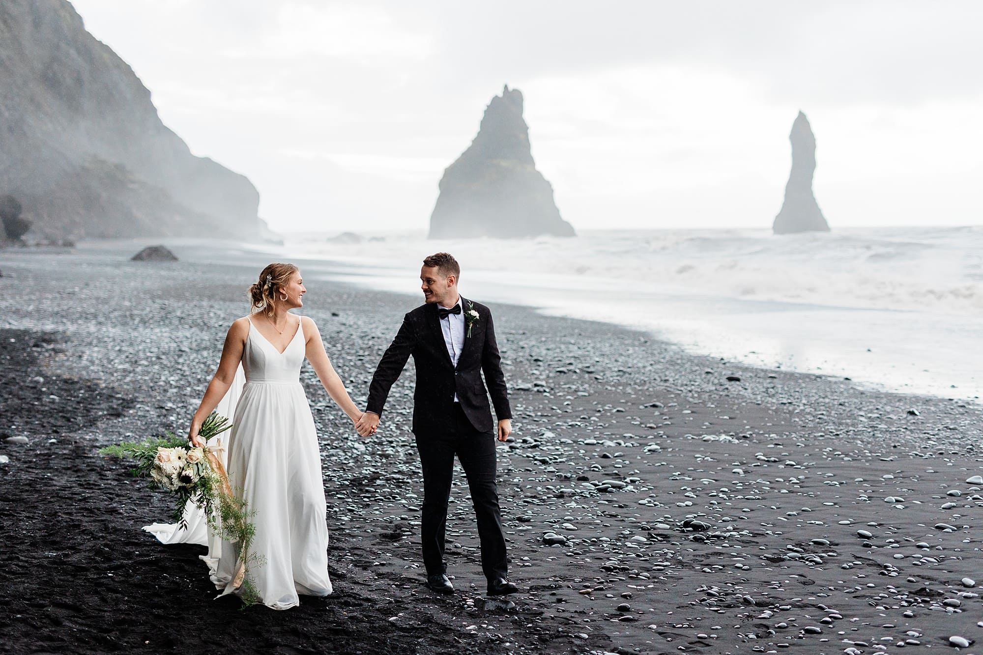 A couple holds hands as they walk on Black Sand Beach after they elope in Iceland