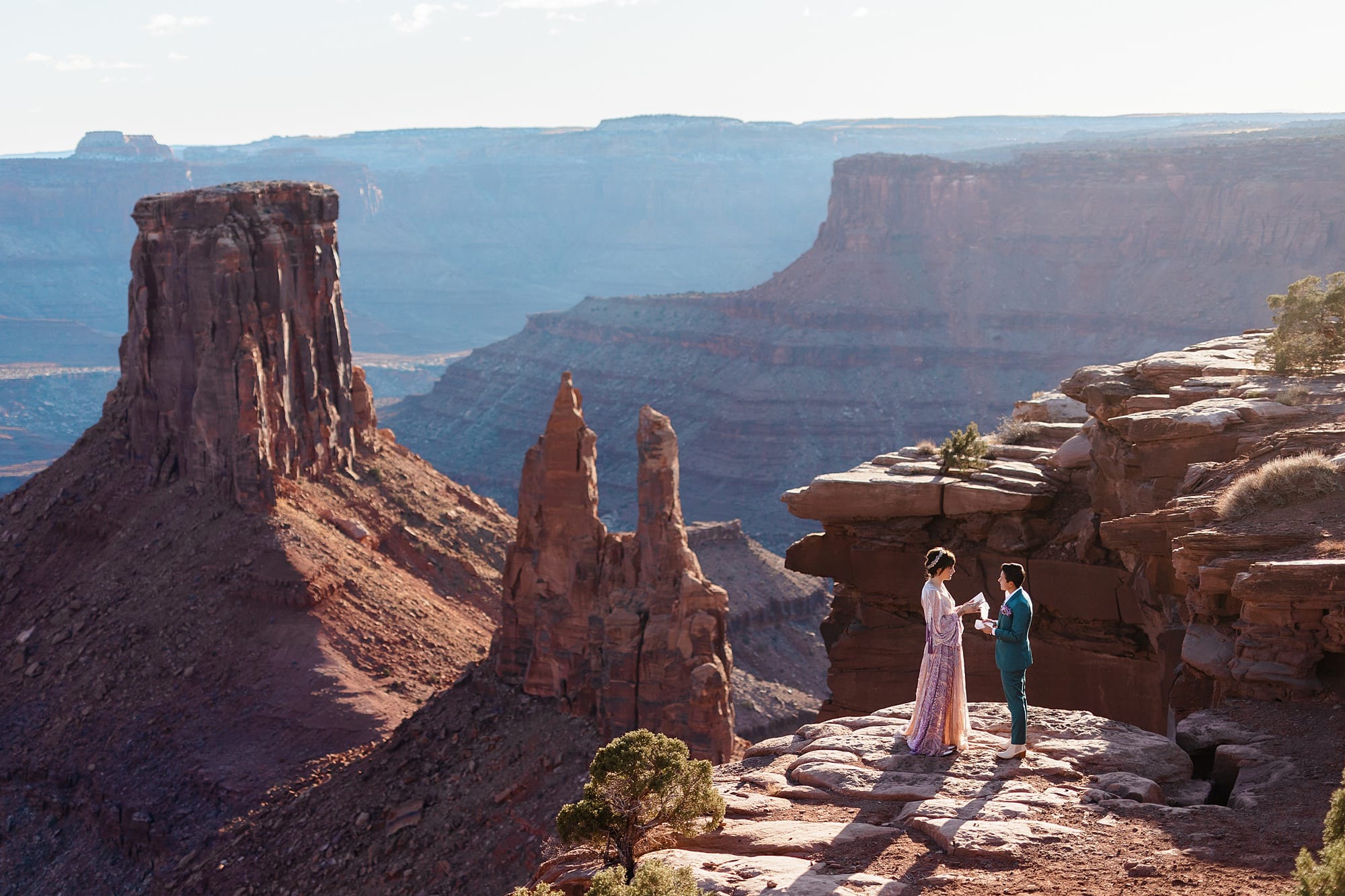 A couple stands on a cliff's edge and reads their vows as they elope in moab.