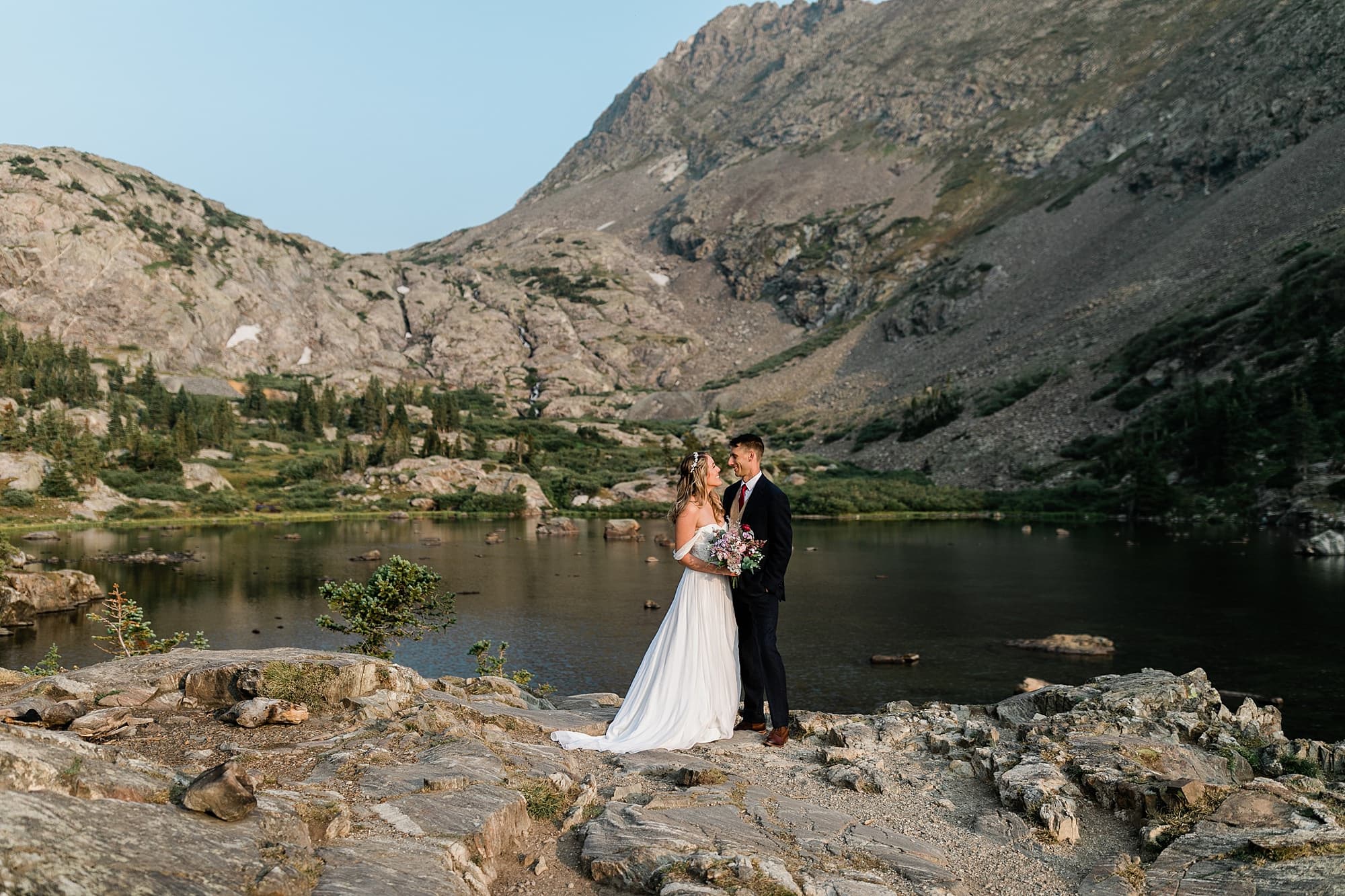 A couple poses in front of a lake in Colorado after their intimate wedding in the Rocky Mountains