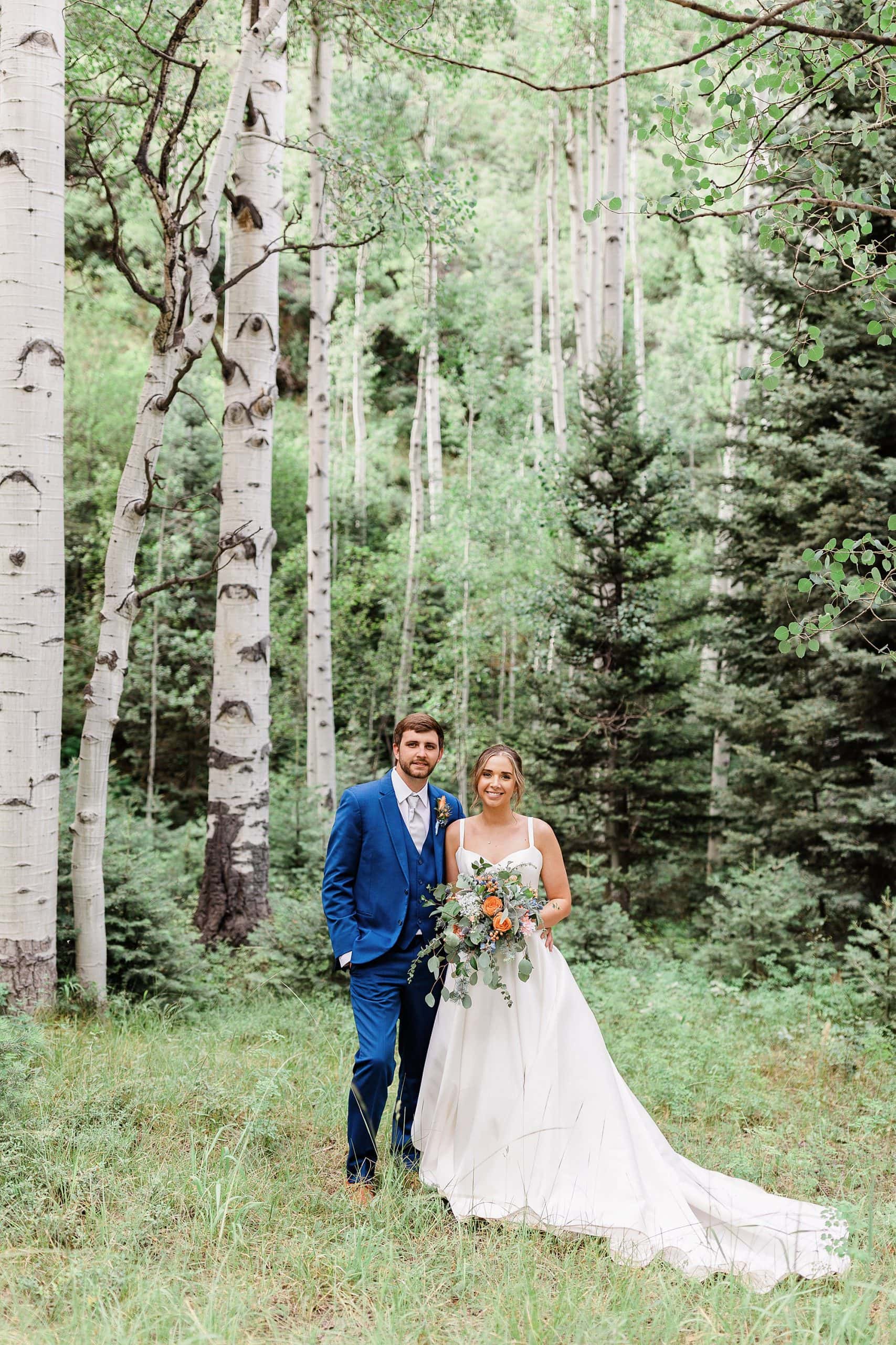 A couple poses in an evergreen forest among Aspens in Colorado