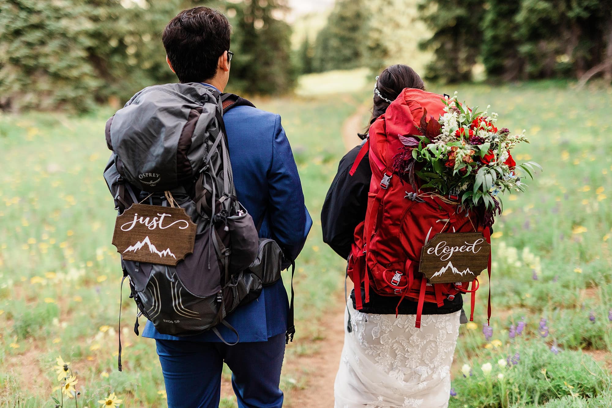 A couple with hiking backpacks have signs that hand and read "just eloped"