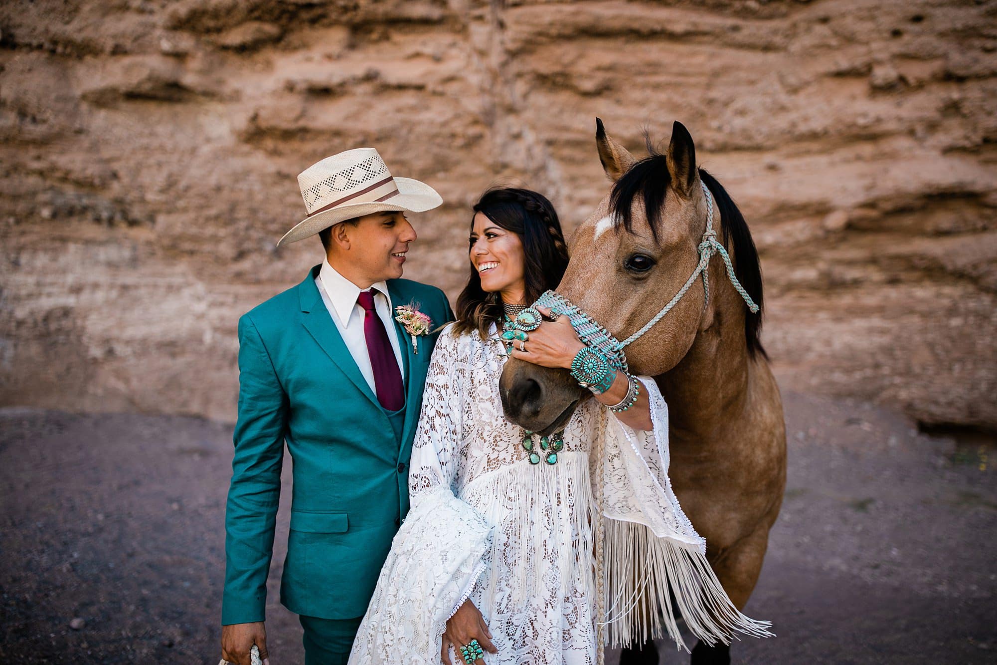 A couple eloping in Albuquerque smiles at each other while petting a horse at their wedding ceremeony 