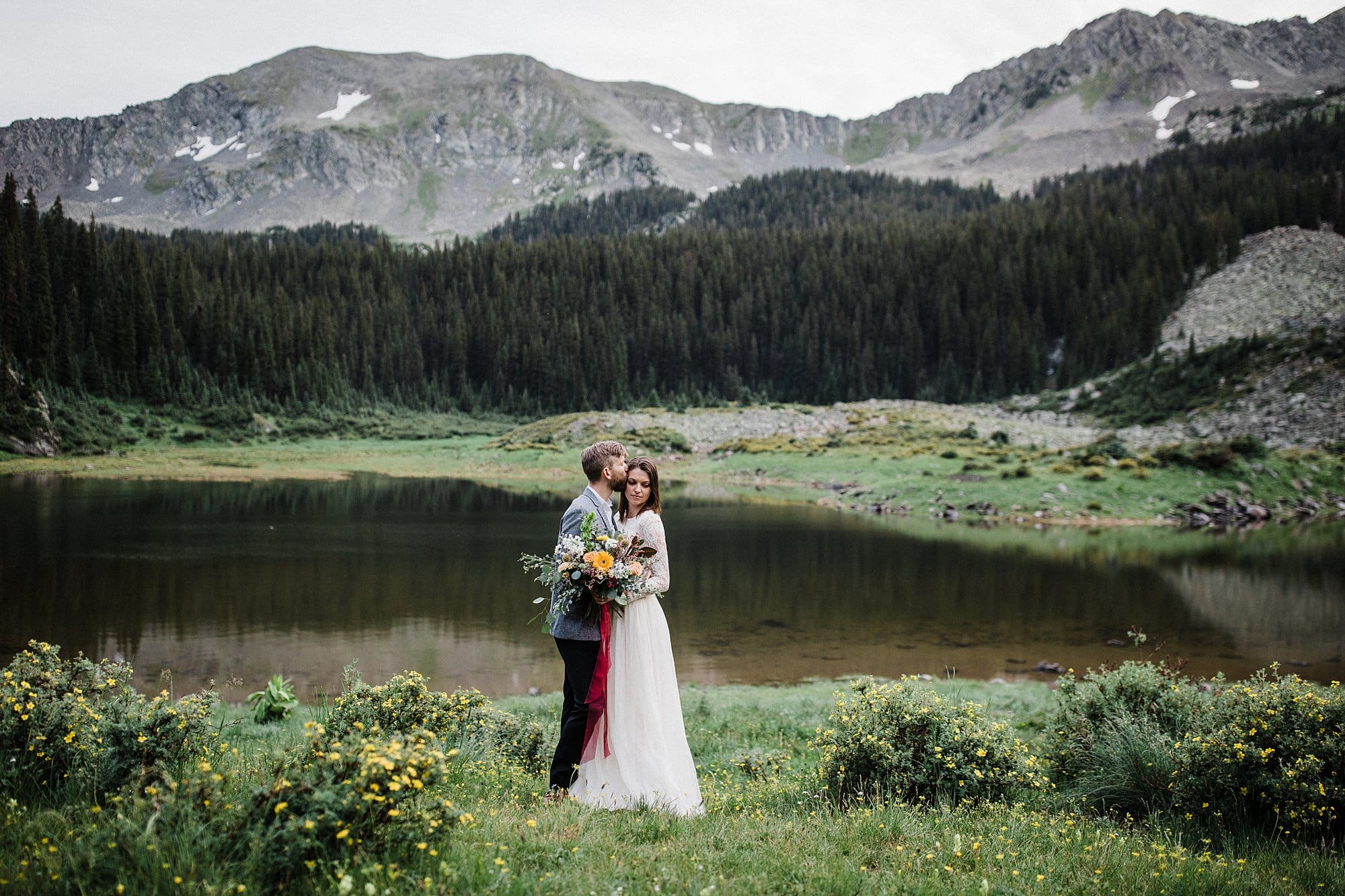A man kisses his bride in front of the Southern Rockies and a lake in Taos 