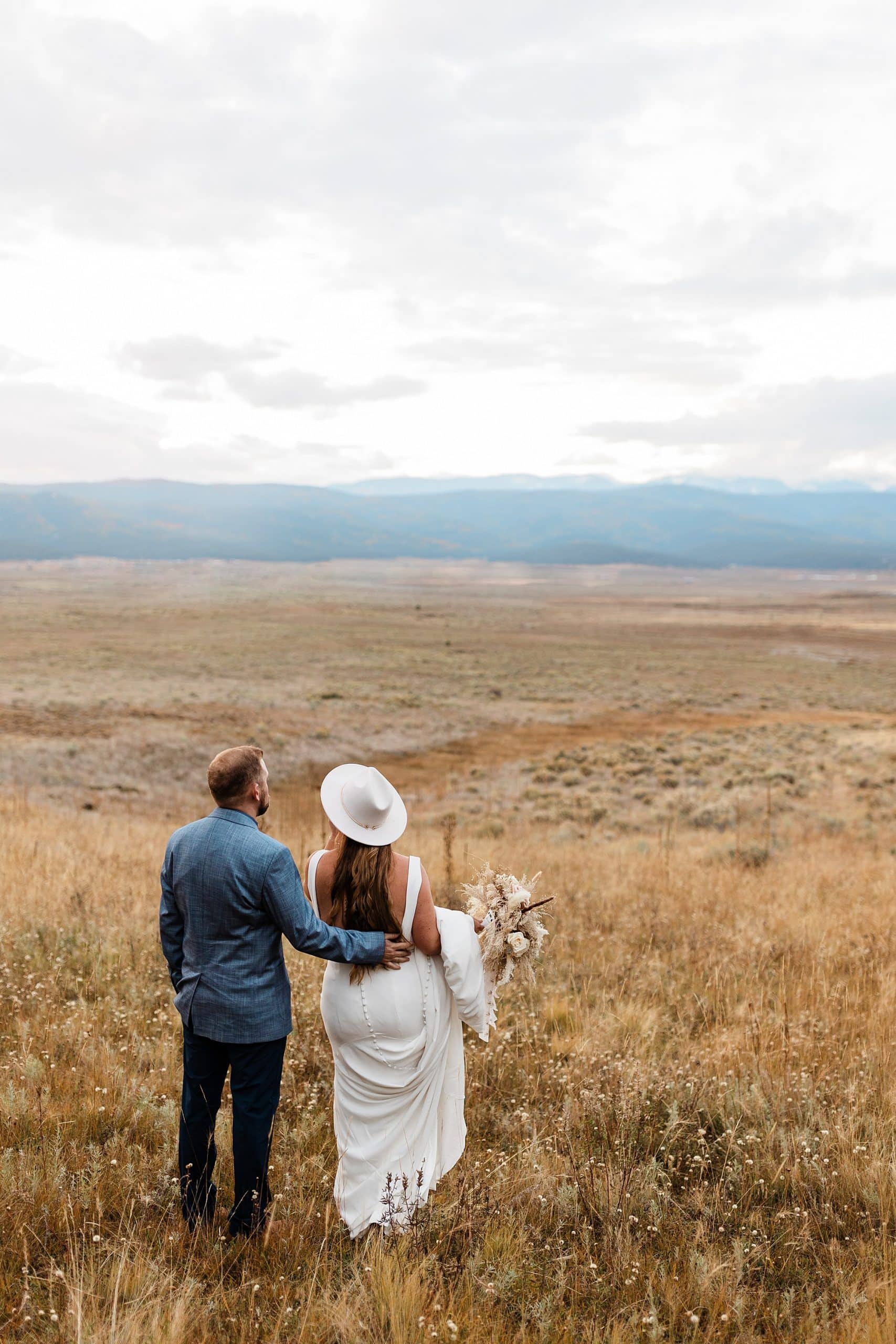 A groom holds his bride's waist as they admire the view of the mountains in Taos. 