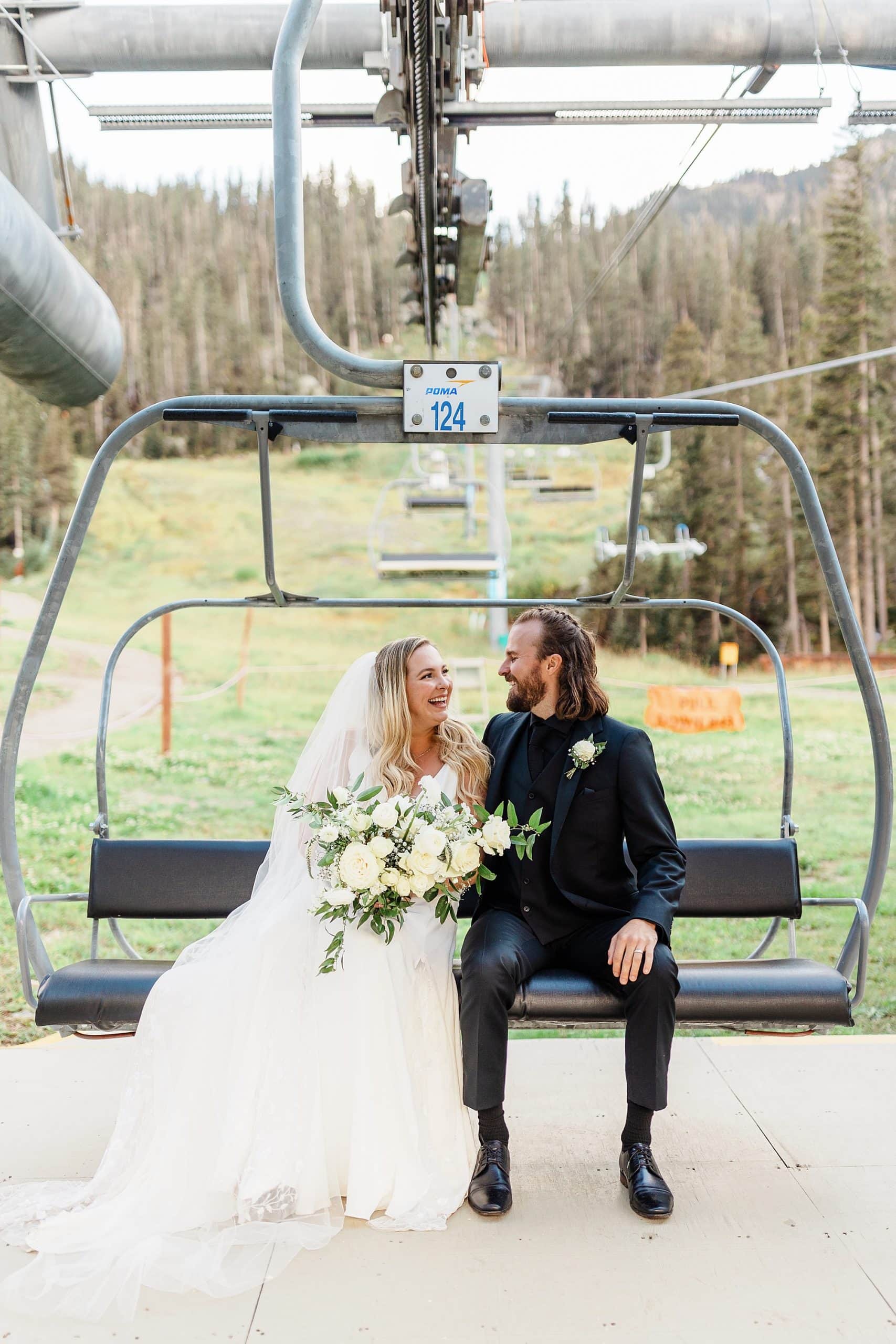 A couple rides a ski lift in Taos Ski Valley in wedding attire. 