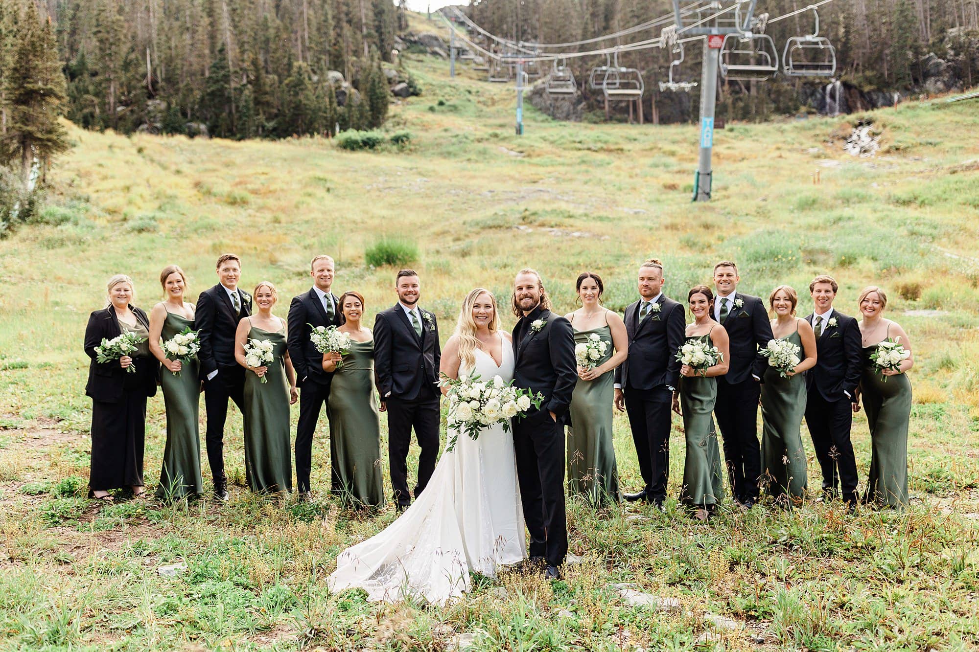 A bride and groom, along with their wedding party, pose in front of a ski lift area in Taos. 