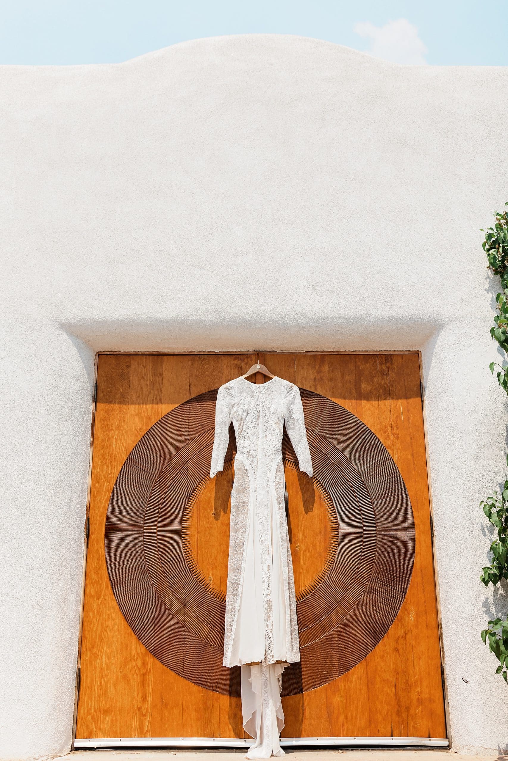 A white wedding dress is displayed against New Mexican architecture. 