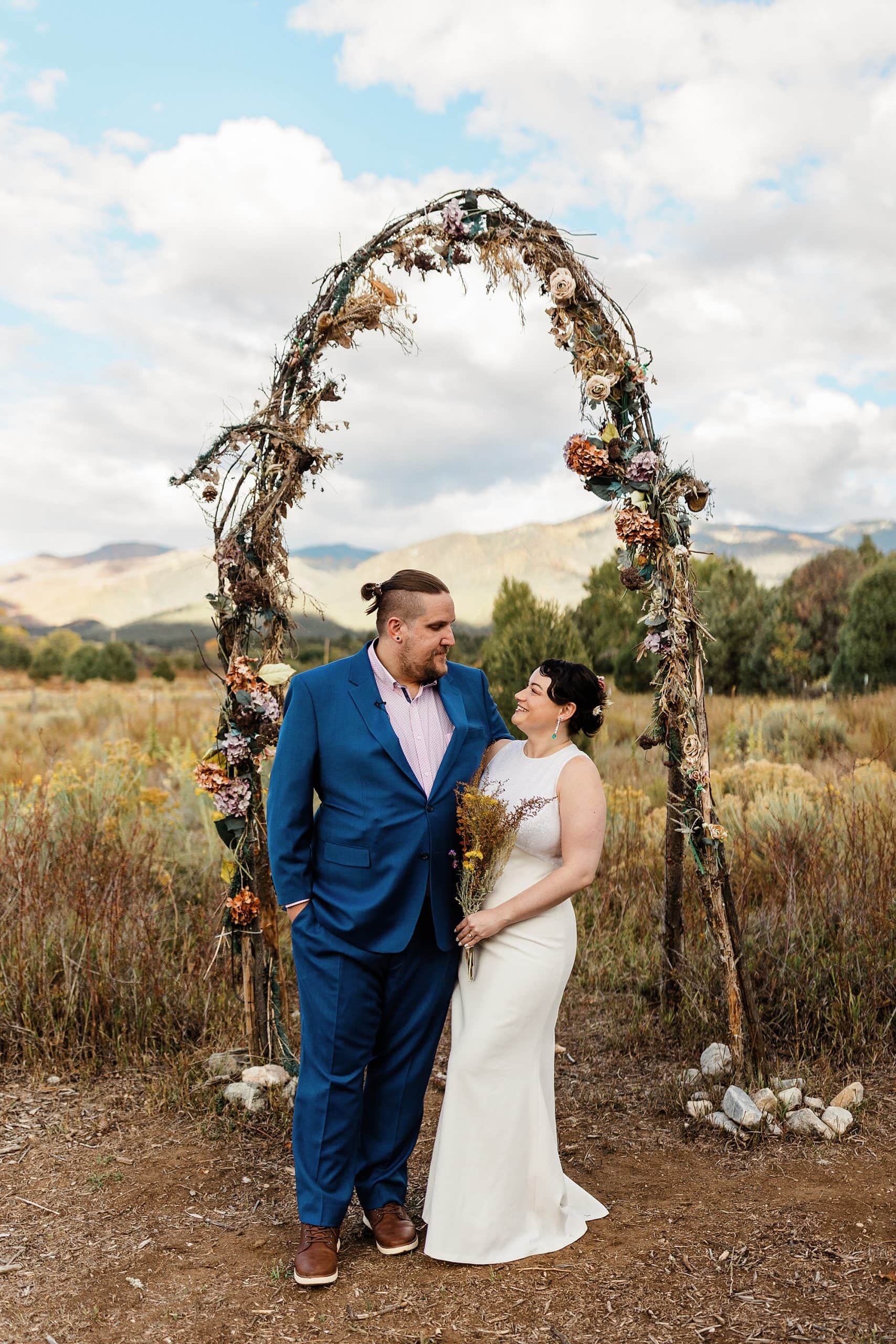 A couple stands in front of a dried floral arch after their elopement in Taos. 